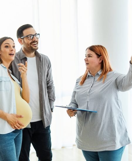Young happy couple, a pregnant woman, and an agent in a new property