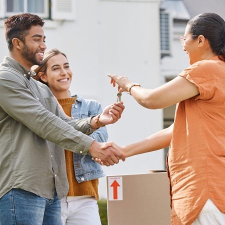 Keys, realtor handshake and couple moving to new house, property investment and mortgage success, deal or thank you. Young people shaking hands and giving lock to dream home and real estate agreement.